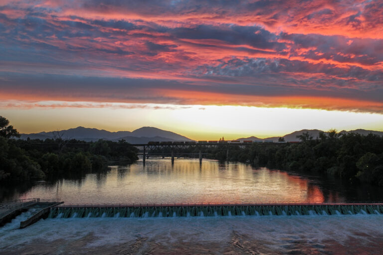 Sacramento River in Redding at sunset looking west with train passing on trestle